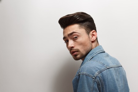 Portrait of handsome young man with bright black hair over white background. Male model in jeans shirt with modern hairstyle in studio.の写真素材