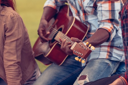 Closeup portrait of Afro-American man playing guitar while spending free time with his best friends on picnic.の写真素材