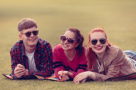 Closeup picture of best friends in sunglasses looking at camera while lying on picnic rug and resting in park.の写真素材