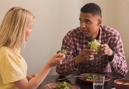 Happy couple eating vegan dishes in vegan restaurant or cafe. People looking at each other while...