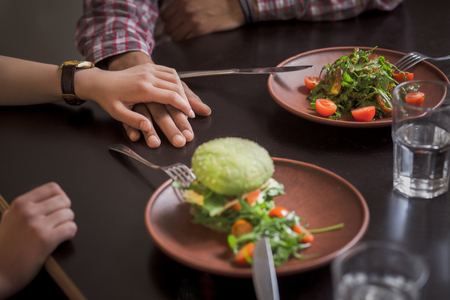 Happy couple eating vegan dishes in vegan restaurant or cafe. Closeup picture of man and woman holding each other's hands.の写真素材