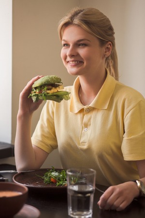 Closeup of lady holding vegan burger in hands while sitting in vegan restaurant or cafe.