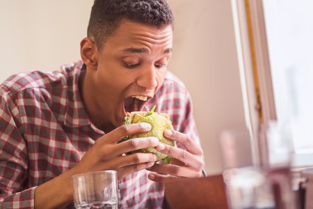 Picture of hungry man eating vegan burger in vegan restaurant or cafe.