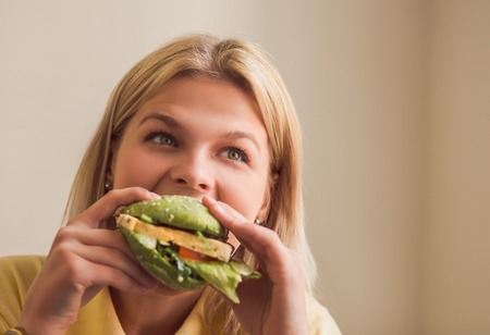 Image of beautiful woman eating vegan burger in vegan restaurant or cafe. Closeup picture of hungry...