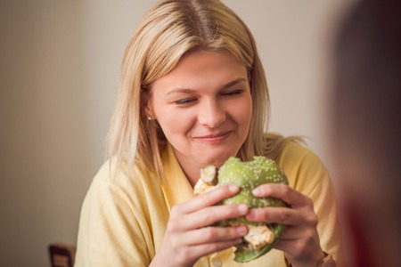 Picture of blond woman eating delicious vegan burger in vegan restaurant or cafe.