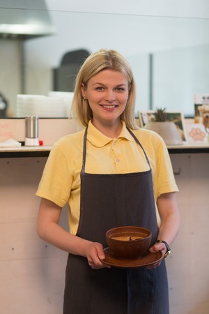 Picture of cook woman from restaurant or cafe holding vegan dish and smiling for camera.