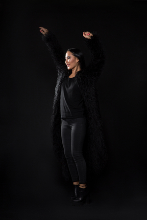 Beautiful lady with black hair posing with her arms raised isolated on black.の写真素材