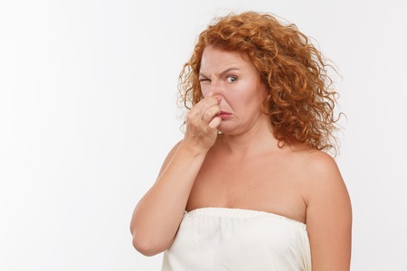 Mature woman holding her nose because of bad smell isolated on white background.の写真素材