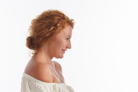 Portrait of happy middle aged woman in white dress in studio. Profile of beautiful lady with red hair posing isolated on white background.の写真素材