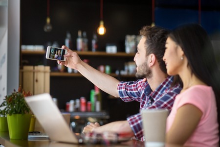 Happy romantic couple posing for camera of mobile or smart phone while having date in restaurant or cafe.の写真素材