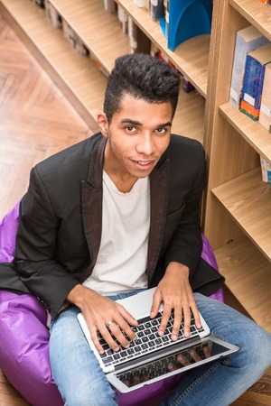 Top view of handsome man working on his laptop computer in library while sitting on the floor near...