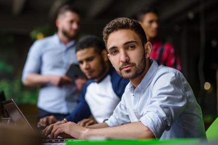 Handsome businessman working on laptop computer in modern office interior. Happy man looking at camera and smiling.の写真素材
