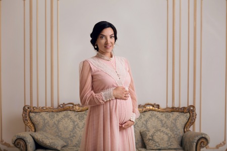 Beautiful pregnant woman in vintage dress posing for photographer. Gentle pretty woman smiling for...