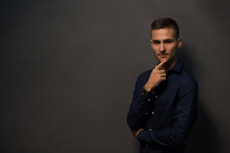Cheerful man with short haircut touching his bearded face and smiling. Fashion or vogue concept. Magazine concept. Happy smiling model man in black shirt looking at camera isolated on black backgroundの写真素材