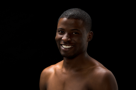 Portrait of happy smiling maked black man posing over black background in studio. Handsome man with short haircut smiling for camera.の写真素材