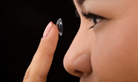 Closeup profile of Korean woman putting on contact lenses over black background. Beautiful lady holding contact lens in front of her.の写真素材