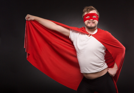 Portrait of comic and funny young super hero man happy smiling in studio. Handsome man with red mask on ready to save world.の写真素材