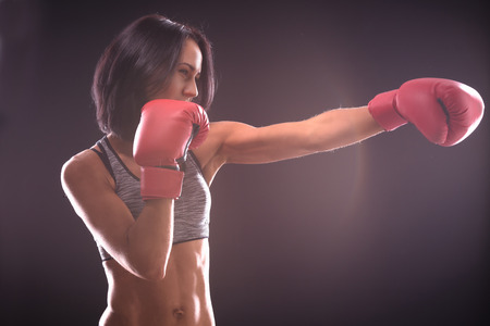 Boxing concept. Profile of fitness or boxer lady with red gloves on practicing direct hits during...