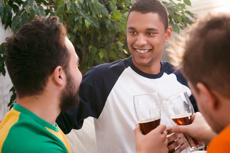 Picture of happy old friends drinking beer, communicating and spending free time at home. Football, party concepts.の写真素材
