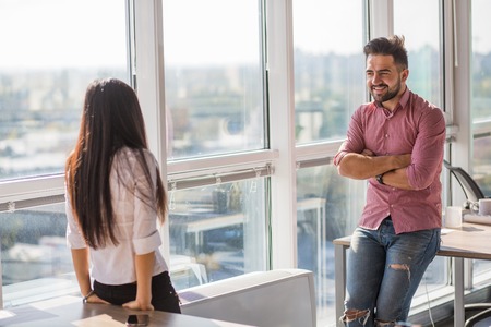 Businessman and businesswoman communicating in office interior all together. Happy colleagues smiling and discussing every day things.の写真素材