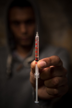 Bad man with syringe using drugs. Drug addict man holding syringe with drugs in front of him. Disease. AIDS. HIV.の写真素材