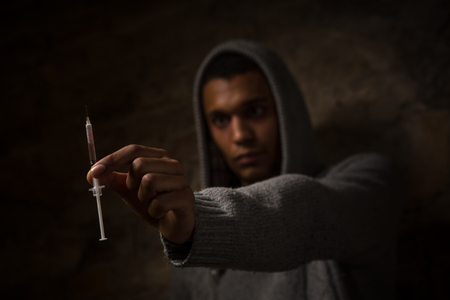Drug addict holding syringe with drugs in front of him. Drugs concept. Disease concept. Drug addict man with syringe using drugs.の写真素材