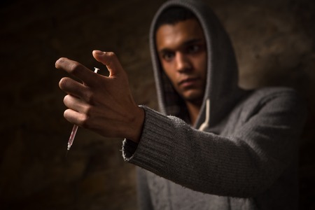 Disease concept. Drug addict man with syringe using drugs. Drug addict holding syringe with drugs in front of him. Drugs concept.の写真素材
