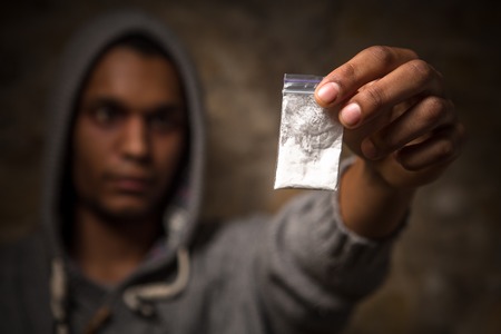 Drug addict varies whether to take drugs in form of white powder. Drug addict showing narcotics and holding them in front of him.の写真素材