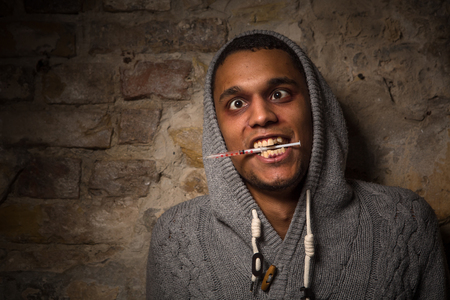 Addict Asian man caught buzz. Drug addict man holding syringe in his mouth isolated on brick background on street.の写真素材