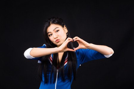 Asian model woman showing heart to camera while posing to photographer and expressing different emotions isolated on black background in studio.の写真素材