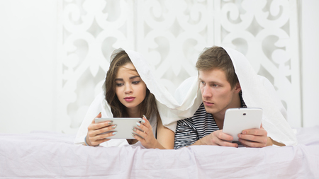 Couple using mobile phone in bedの写真素材