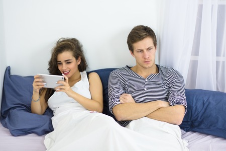 Couple using mobile phone in bedの写真素材