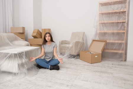 Young female sitting in relaxation pose on the floor after relocation to new home.