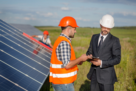Businessman signing contract with foreman, technician examining solar panels at backdrop.の写真素材