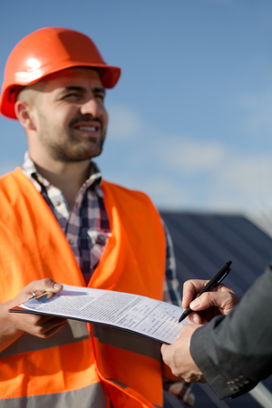 Foreman in orange helmet and vest holding documents for signature.の写真素材