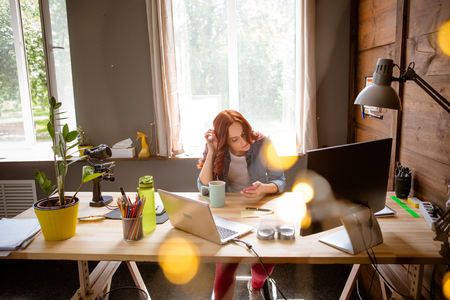 Freelancer woman sitting at table, holding mobile phone in hands.の写真素材