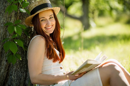 Romantic young lady in straw hat reading a book sitting in garden.の写真素材