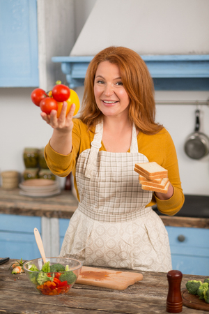 Portrait of housewife standing in kitchen holding colorful vegetables.の写真素材