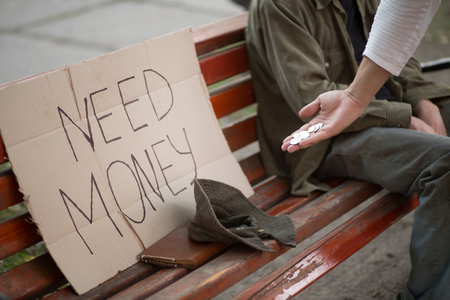 Image of bench with cardboard with sign need money, hat and hand with coins.の写真素材