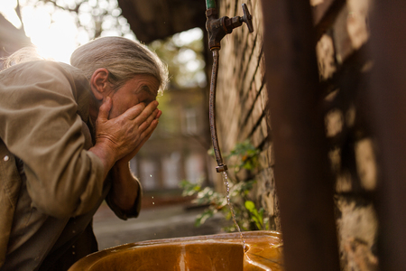 Old homeless tramp with long grey hair washing face.の写真素材