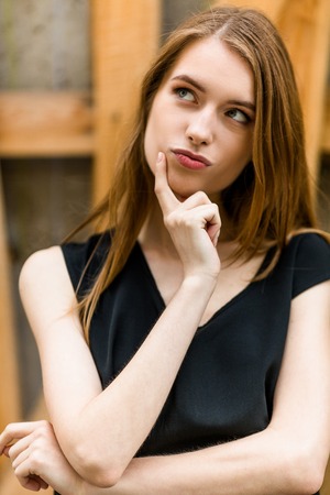 Beautiful young female dreaming outdoors. Attractive girl with long hair touching face with forefinger.の写真素材