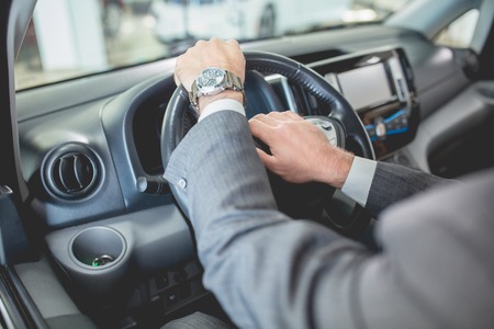 Mans hands on steering wheel of new electro car. Buyer examining new vehicle in auto showroom.の写真素材