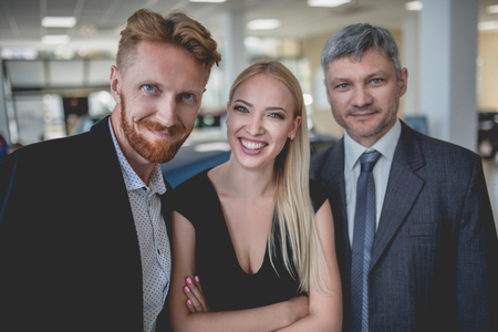 Happy young couple and vehicle dealer in auto showroom. Man and woman choosing new car.の写真素材