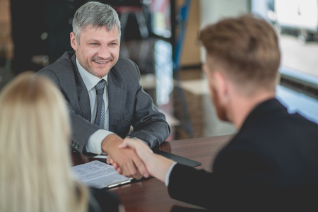 Auto dealer agent signing purchasing contract with a buyer, shaking hands. Buying new car concept, buyers and manager making deal.の写真素材