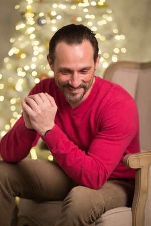 Sexy smiling man in red sweater sitting in arm chair.の写真素材