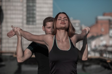 Man and woman working out outdoors. Fitness on the roof concept, man helping young female to stretch...