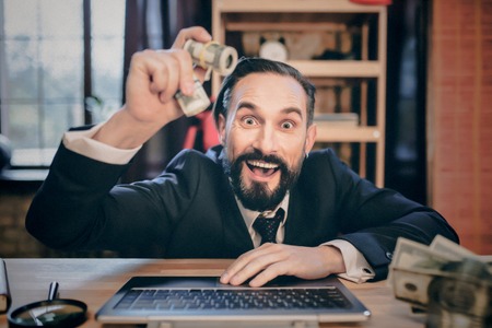 smiling businessman sitting on laptop and demonstrating money on camera.の写真素材
