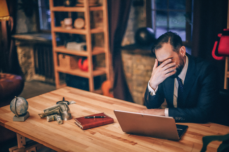 Close up of sad businessman sitting at desk in his luxury office.の写真素材