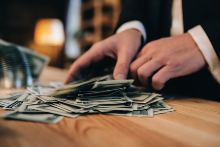 Dollar banknotes on wooden desk. Hands of man touchinh money.の写真素材
