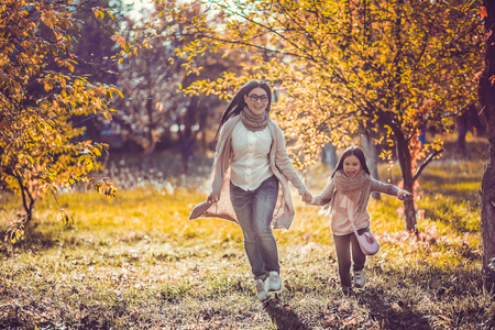 Beautiful mum and daughter happily spend time in autumn garden.の写真素材